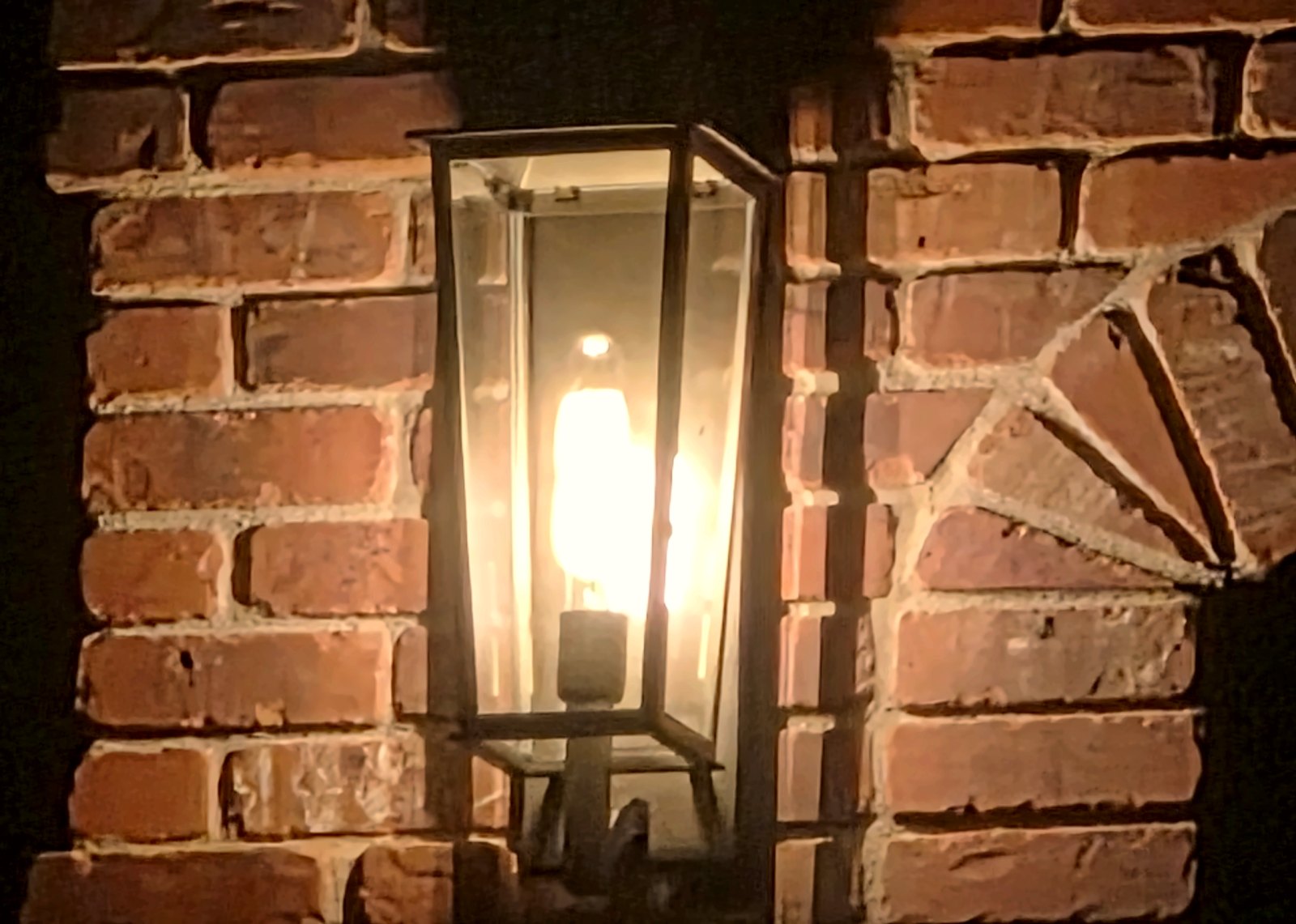 Black lantern wall sconce installed on brick exterior